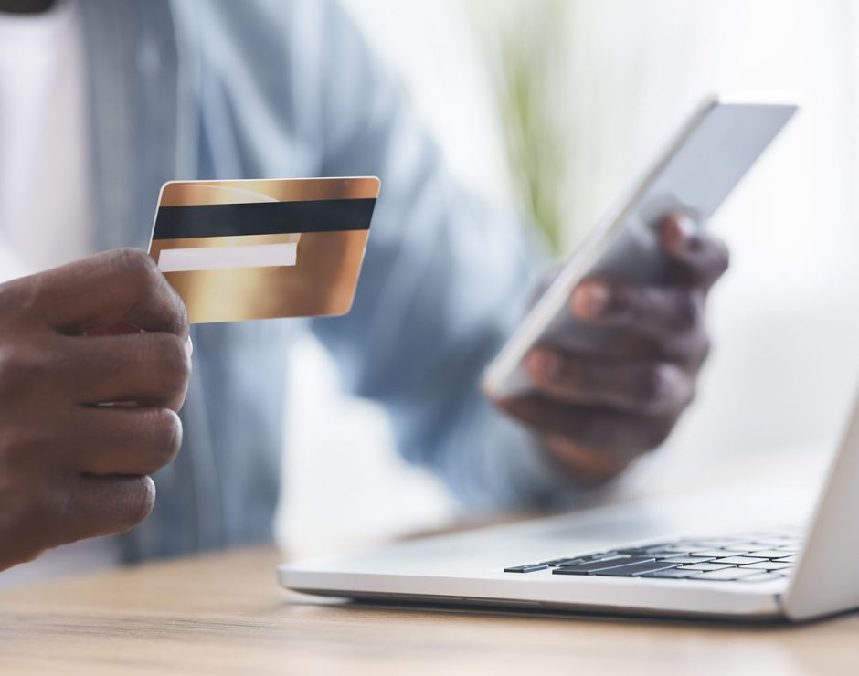 Online payment. Unrecognizable african american man using credit card and smartphone for paying bills in internet, closeup