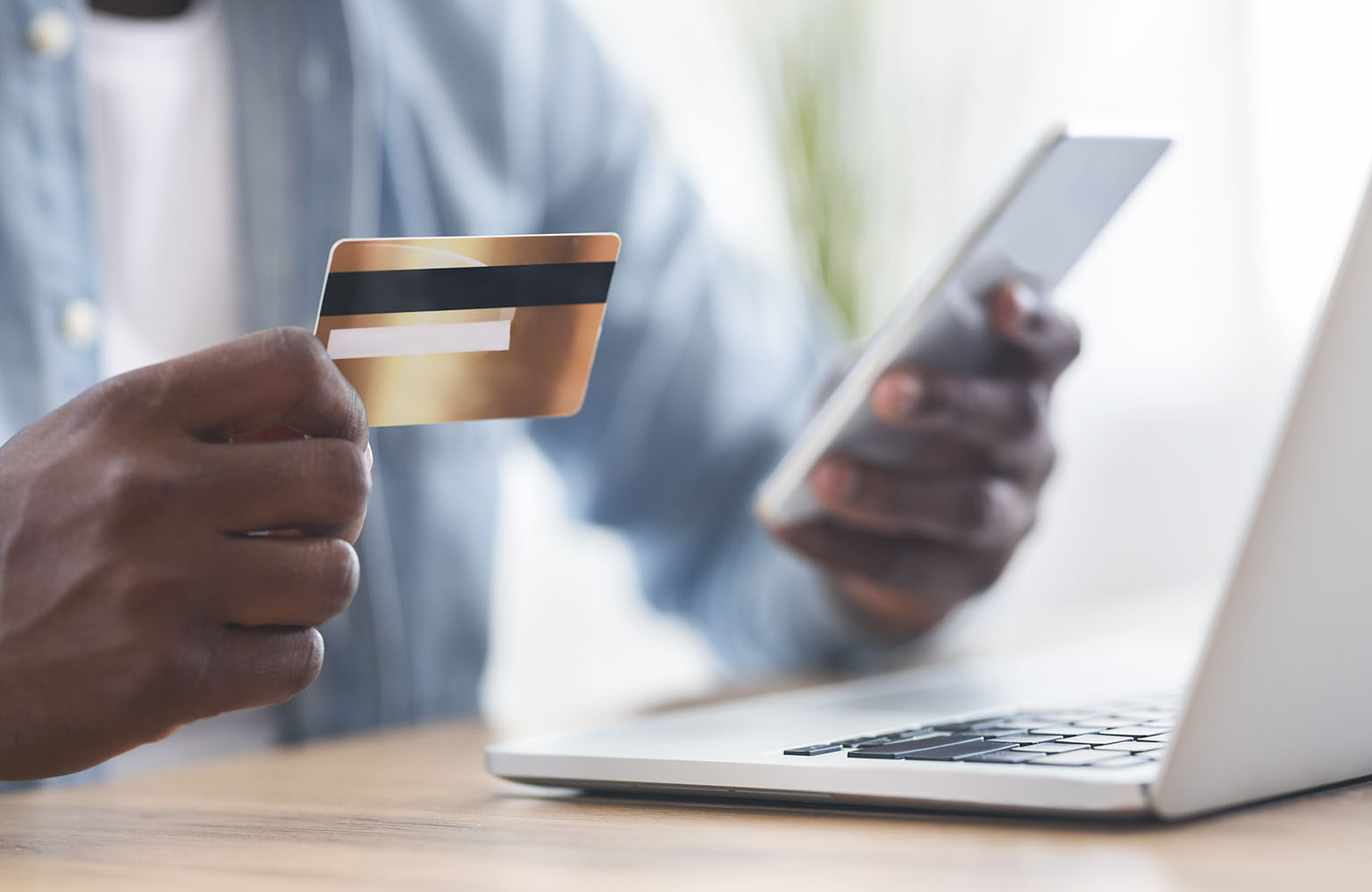 Online payment. Unrecognizable african american man using credit card and smartphone for paying bills in internet, closeup